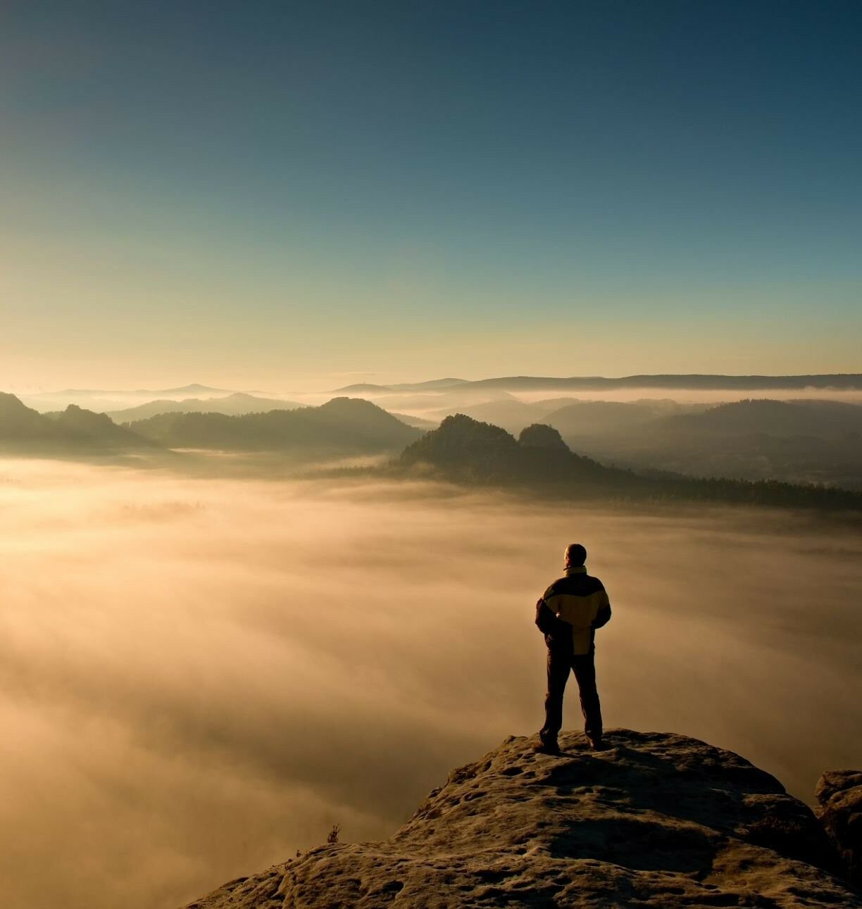 Man stands on the peak of sandstone rock in national park Saxony Switzerland and watching to Sun. Beautiful moment the miracle of nature